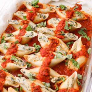 A rectangular glass pan with vegan stuffed shells in marinara topped with fresh basil.