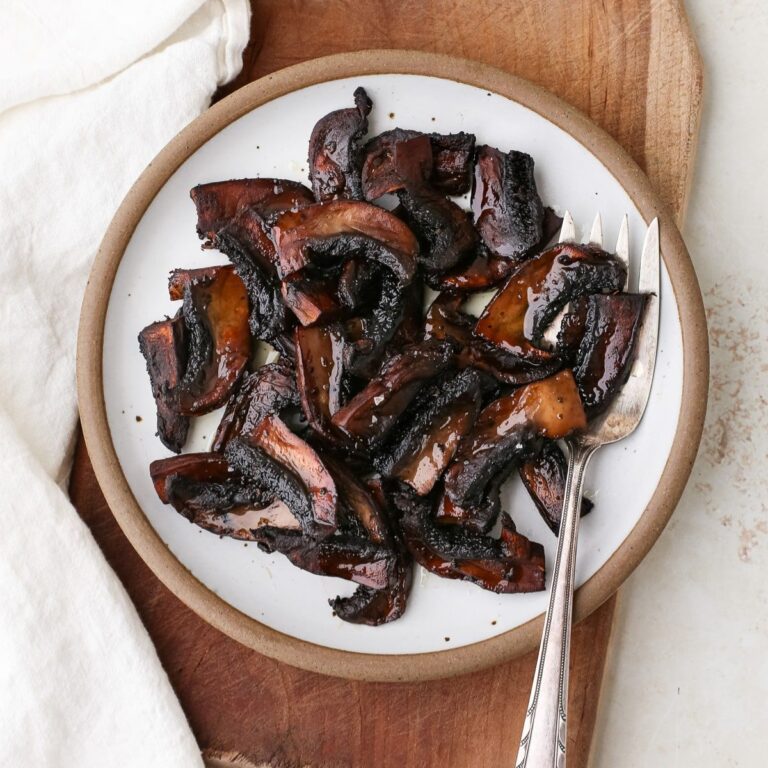 Caramelized marinated portobello mushrooms on a plate with a serving fork.