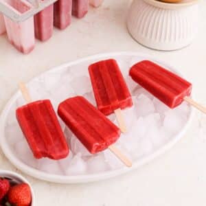 Homemade strawberry grapefruit popsicles on ice on a plate.
