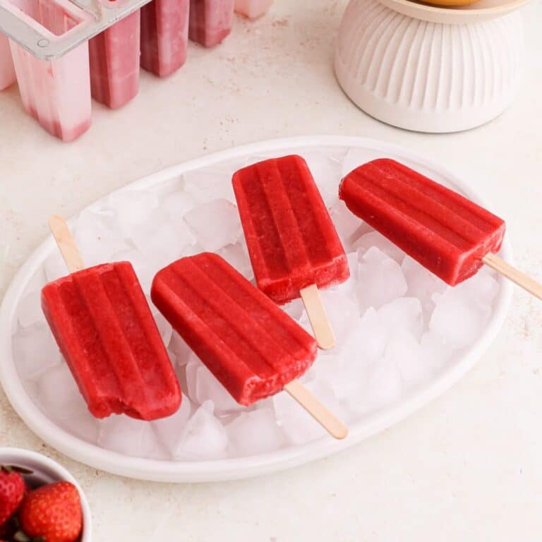 Homemade strawberry grapefruit popsicles on ice on a plate.