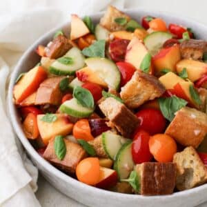 A large round bowl of colroful peach panzanella salad.