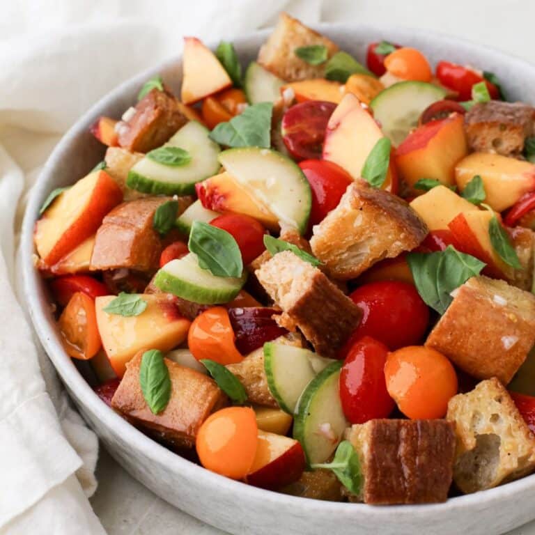 A large round bowl of colroful peach panzanella salad.