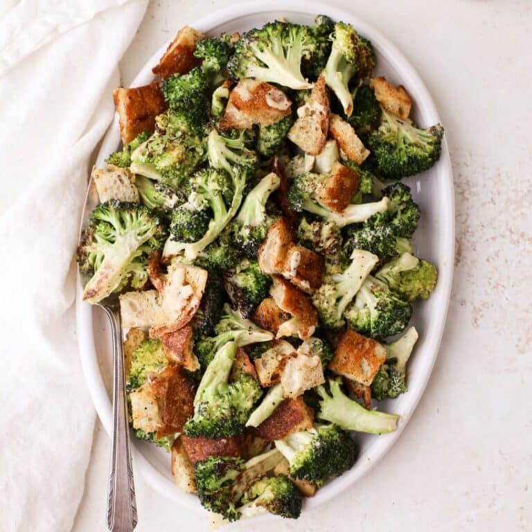 An oval plate with broccoli caesar salad next to a jar of homemade dairy free caesar dressing.