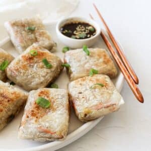 Crispy rice paper dumplings on a serving platter with dipping sauce and chopsticks.
