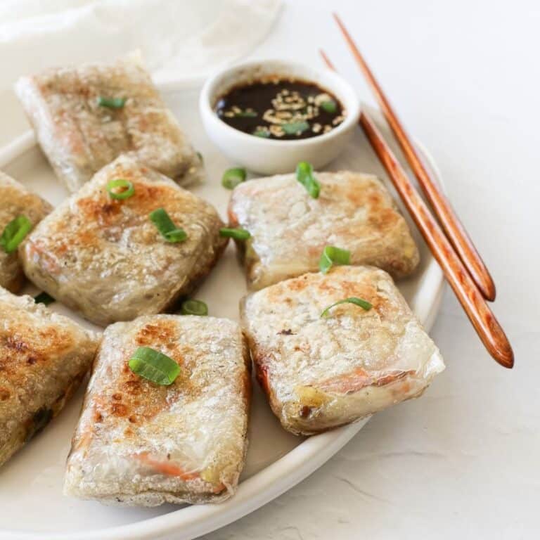 Crispy rice paper dumplings on a serving platter with dipping sauce and chopsticks.