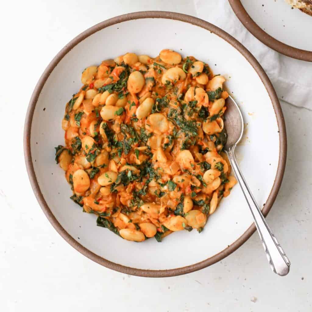 Two bowls of creamy harissa butter beans with kale and a side of toast.