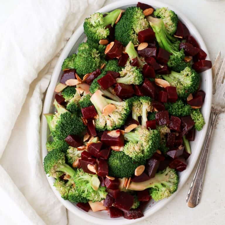 Beet and broccoli salad with toasted sliced almonds on an oval plate.