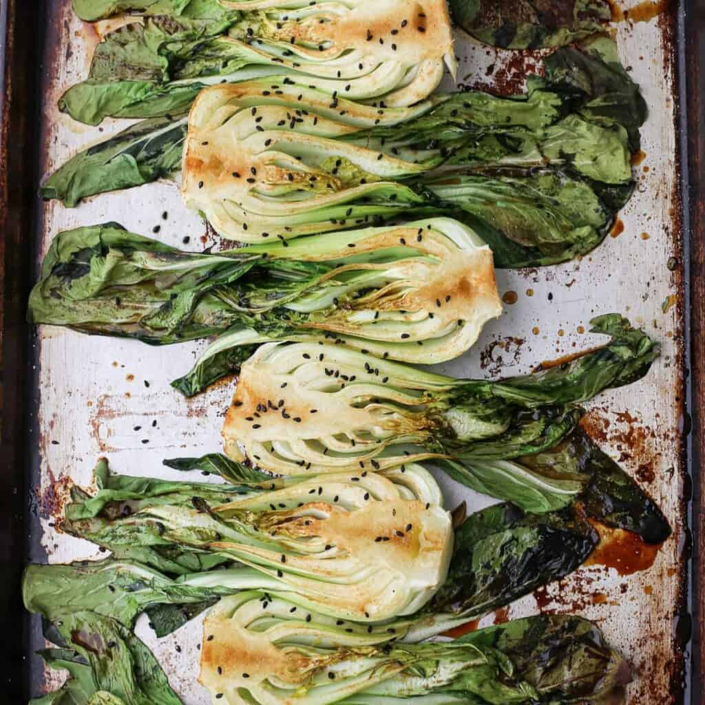 Oven roasted bok choy on a sheet pan topped with black sesame seeds.
