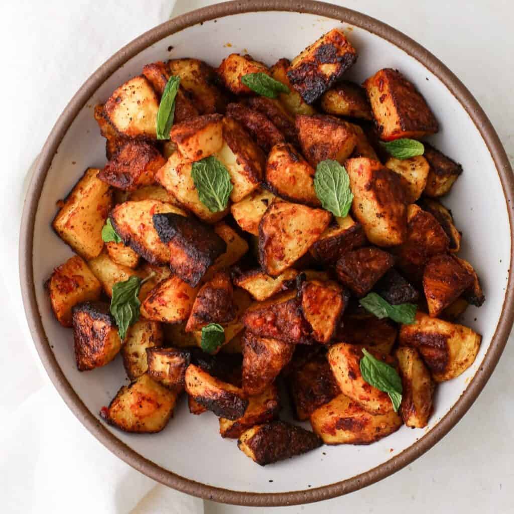 A bowl of roasted harissa potatoes with fresh mint leaves.