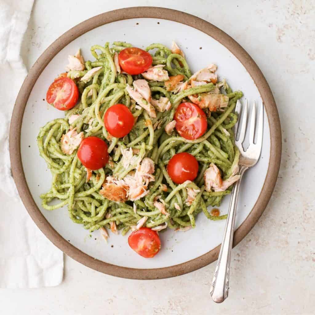 Plates of salmon pesto pasta with halved cherry tomatoes.