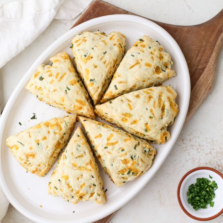 Cheese and chive scones on an oval plate next to a small bowl of minced fresh chives.