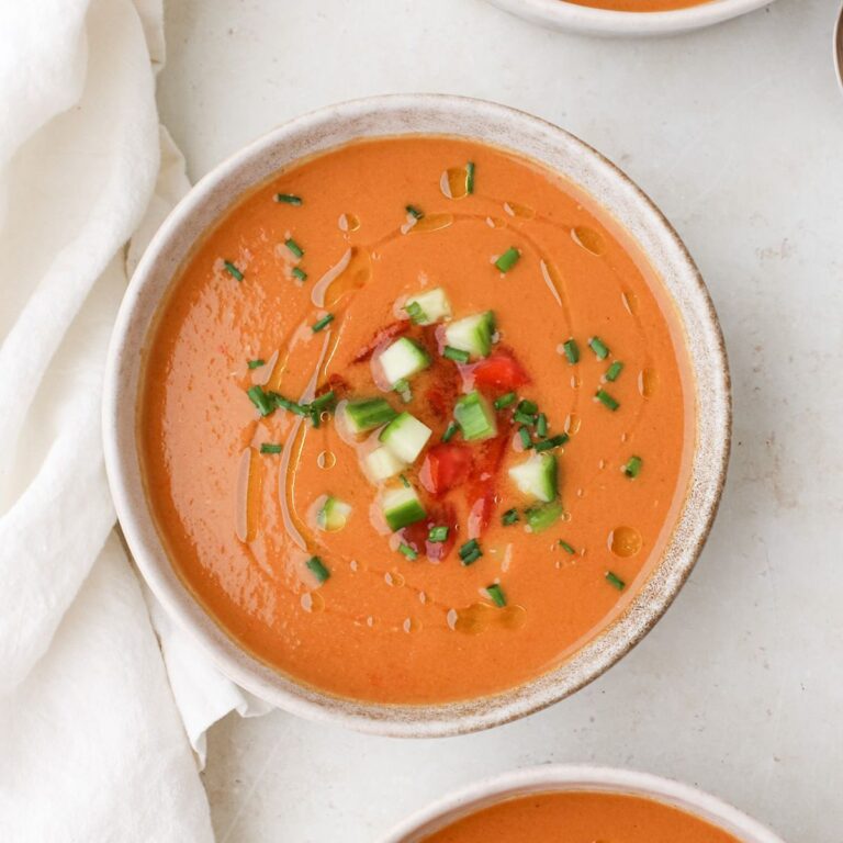 Three bowls of tomato watermelon gazpacho with chopped chives, tomatoes, and cucumber.