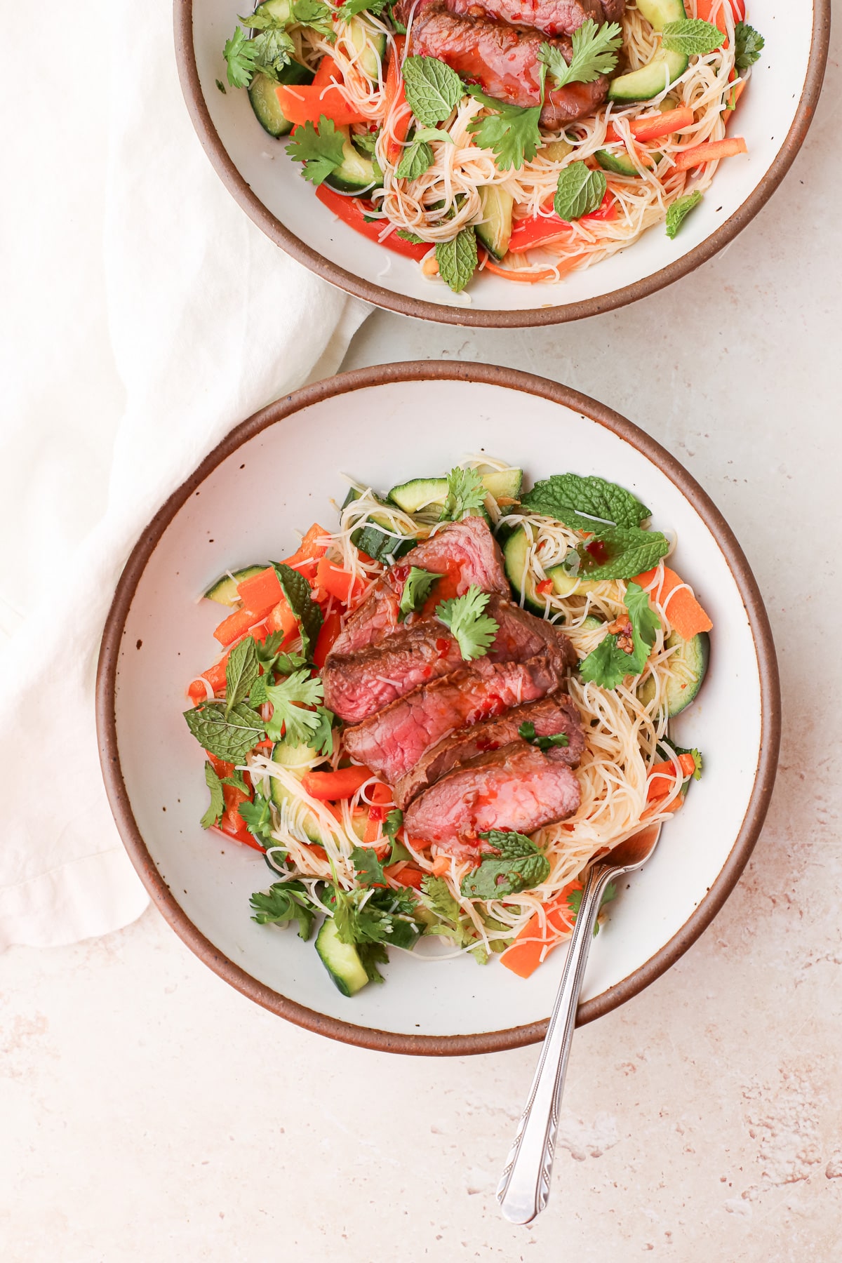 Two bowls of Thai beef noodle salad with fresh mint and cilantro.