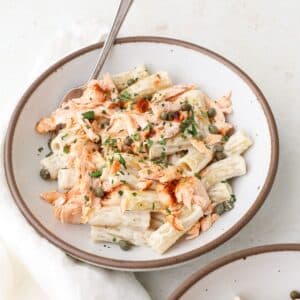Two bowls of salmon pasta with capers and fresh parsley.