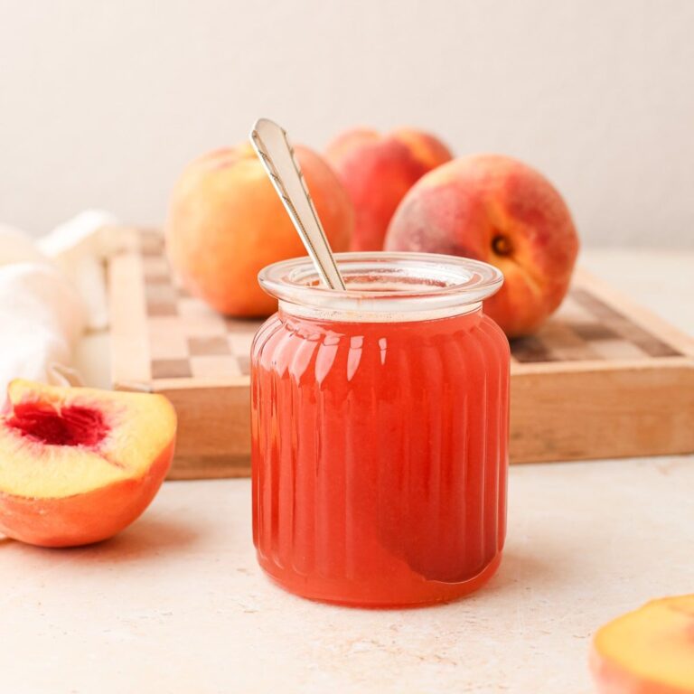 A beautiful jar of homemade peach simple syrup with fresh peaches.