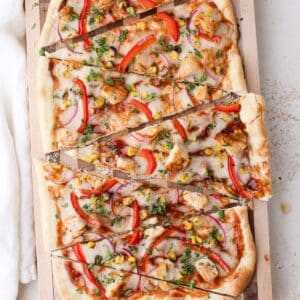 Sliced bbq chicken flatbread on a checkered cutting board topped with cilantro.