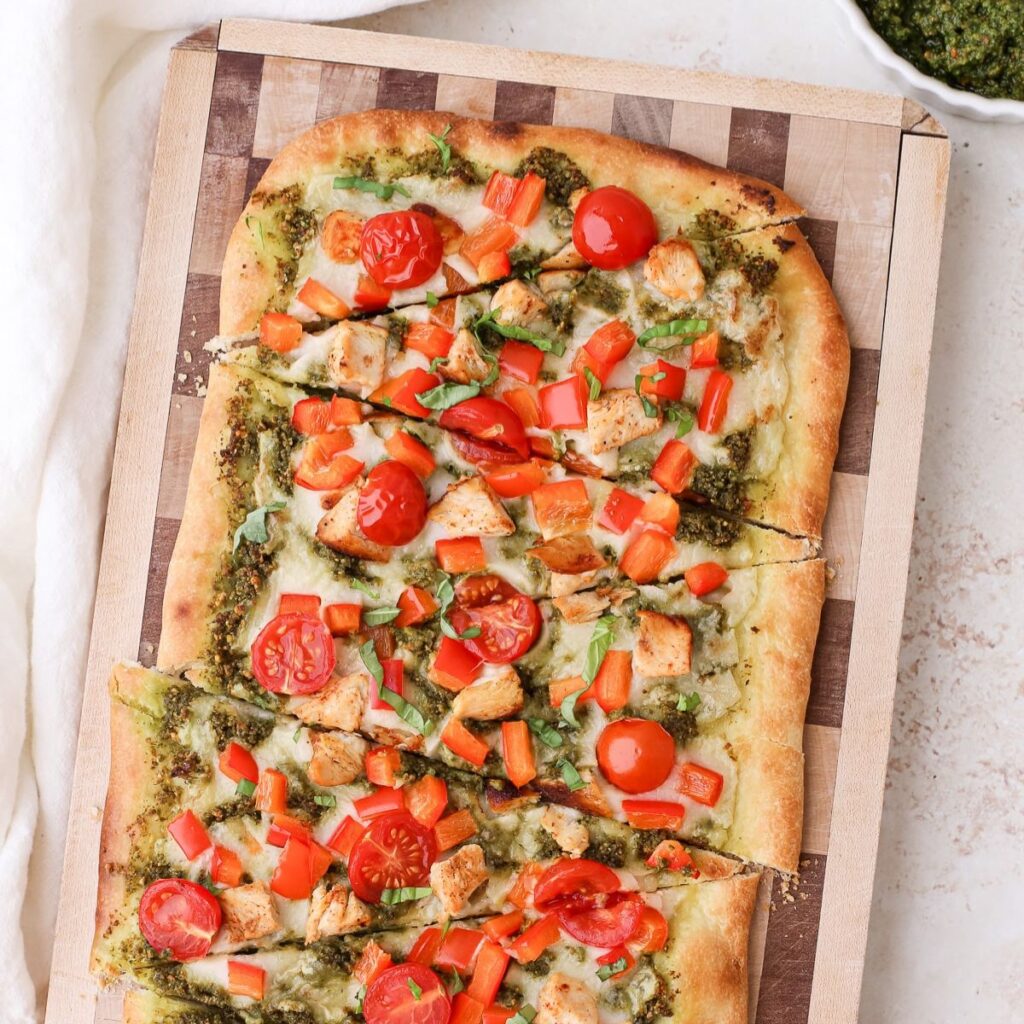 Homemade pesto chicken flatbread with cherry tomatoes and diced red bell pepper.