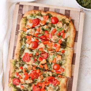 Homemade pesto chicken flatbread with cherry tomatoes and diced red bell pepper.