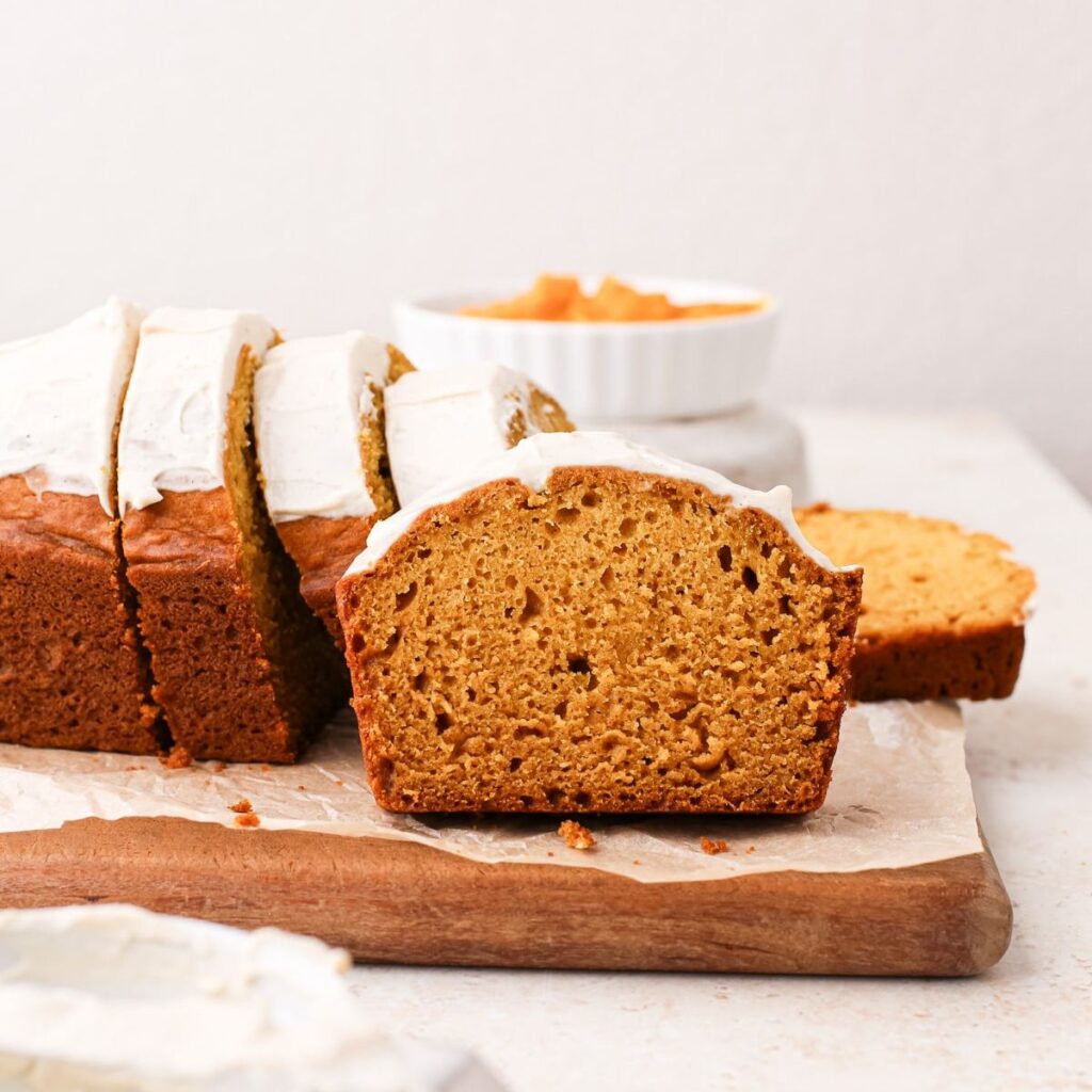 Slices of pumpkin olive oil cake with vanilla cinnamon yogurt topping on a cutting board.