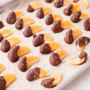 A parchment paper lined baking sheet with chocolate dipped orange segments topped with flaky salt.
