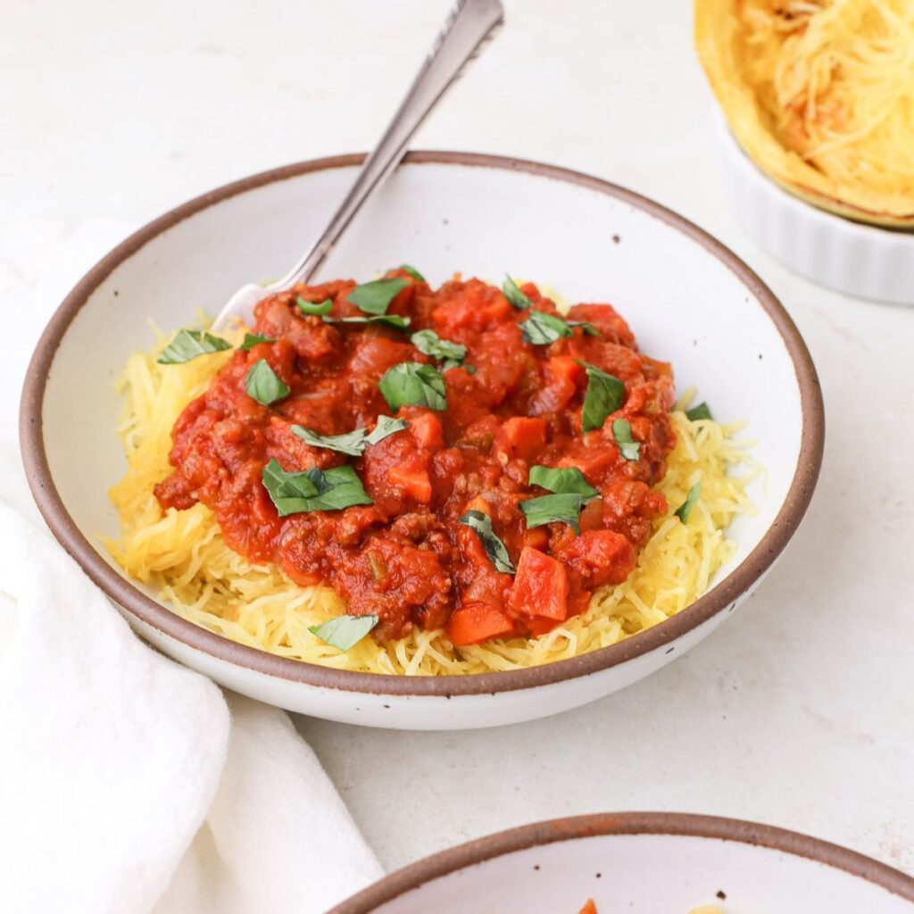 Two bowls of homemade spaghetti squash bolognese topped with torn fresh basil leaves.