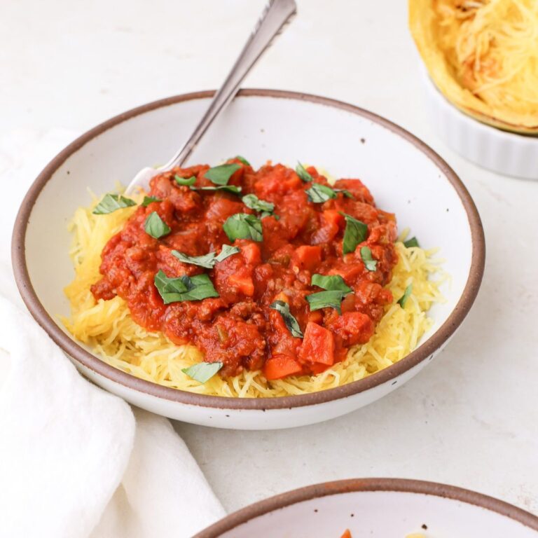 Two bowls of homemade spaghetti squash bolognese topped with torn fresh basil leaves.