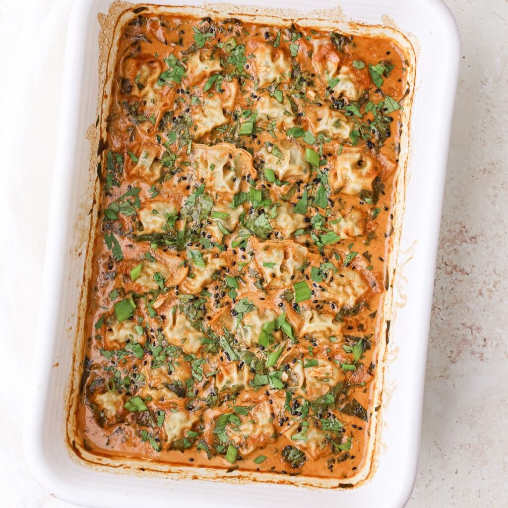 A 9x13 ceramic baking dish with red curry baked dumplings garnished with sliced green onions, chopped cilantro and black sesame seeds.