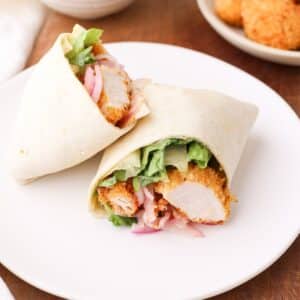 Crispy chicken wrap on a plate with romaine lettuce, quick pickled red onion, and spicy honey mustard sauce.