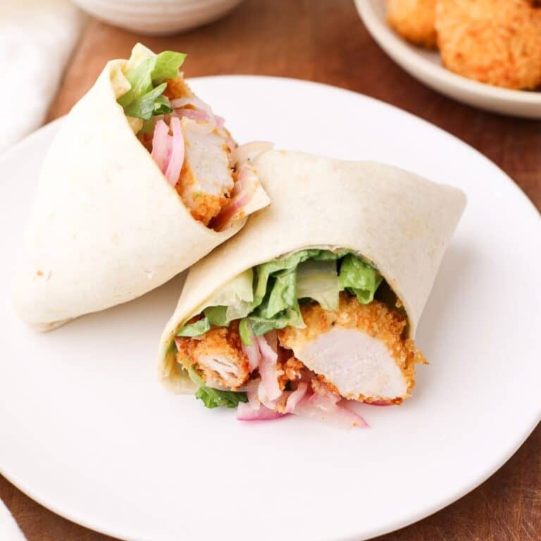 Crispy chicken wrap on a plate with romaine lettuce, quick pickled red onion, and spicy honey mustard sauce.