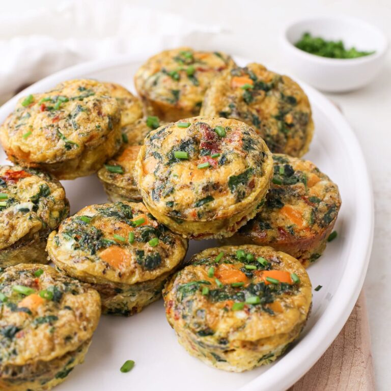 Dairy free egg bites with sun dried tomatoes, chopped orange bell pepper, and spinach on an oval plate topped with chives.