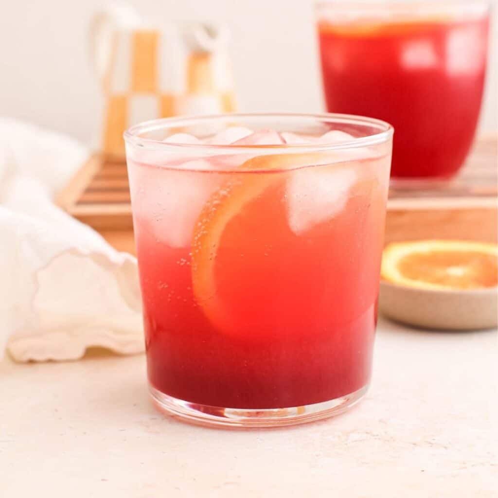 Two blood orange mocktails with hibiscus syrup, sparkling water, and ice cubes plus a blood orange slice.