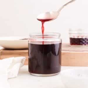 A jar of homemade hibiscus syrup with syrup running off of a spoon into the jar.