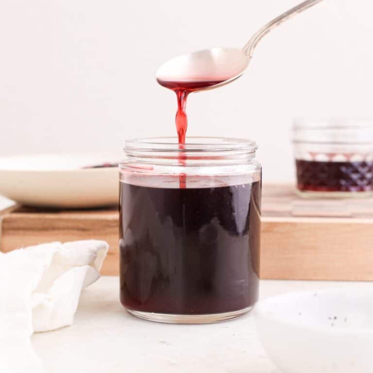 A jar of homemade hibiscus syrup with syrup running off of a spoon into the jar.