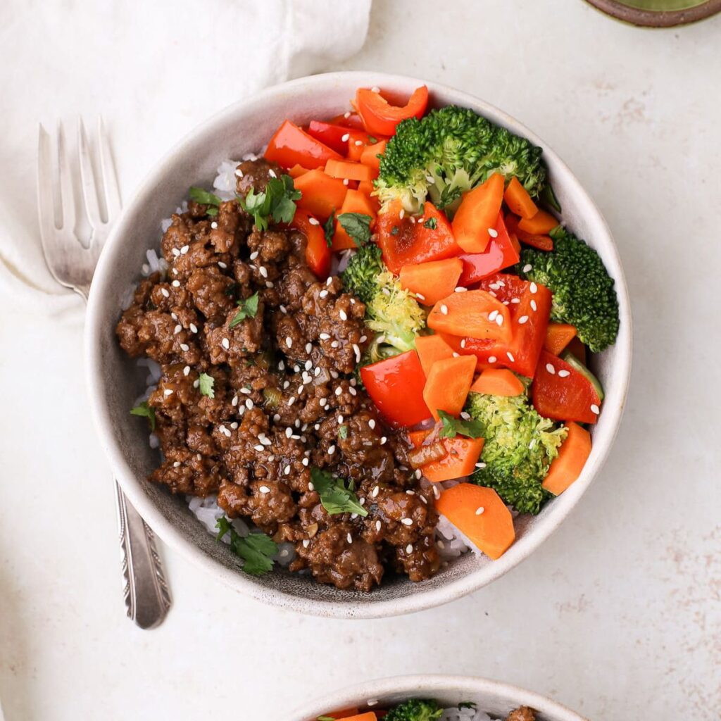 Beef teriyaki bowls with cooked white rice, ground beef, homemade teriyaki sauce, broccoli, carrots, and red bell pepper topped with white sesame seeds and cilantro.