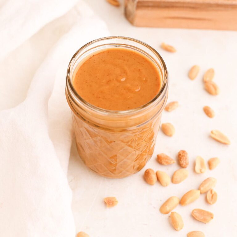 A jar of homemade thai peanut sauce surrounded by roasted peanuts.