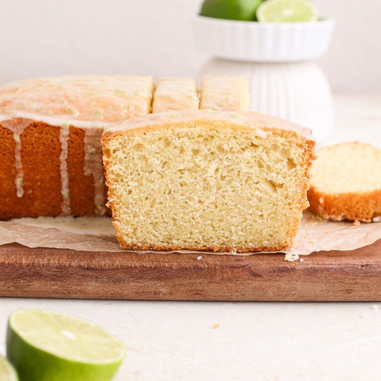 A lime cake loaf with a zesty lime glaze on a cutting board next to fresh limes.