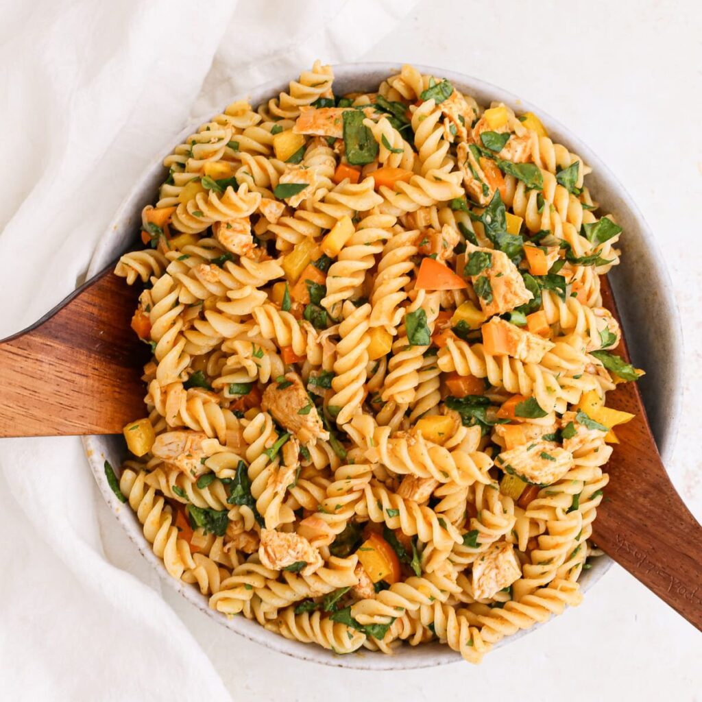 A large bowl of curry pasta salad with wooden salad servers.
