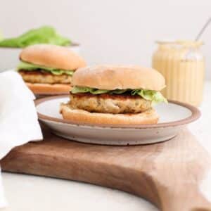 Chicken caesar burgers on a plate next to a jar of homemade caesar dressing with a spoon in it.