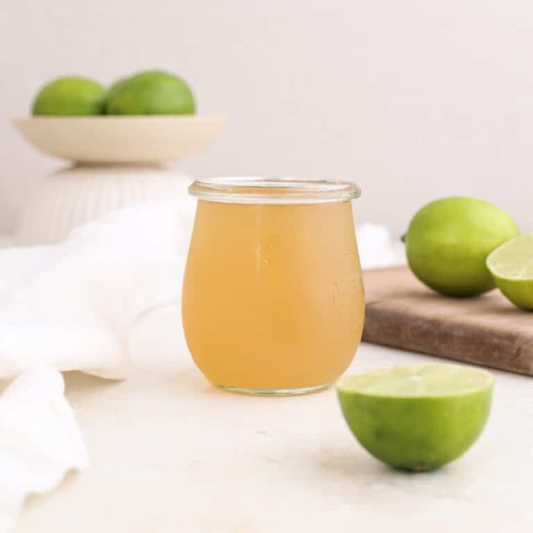 A jar of homemade lime syrup on a cutting board next to fresh limes.