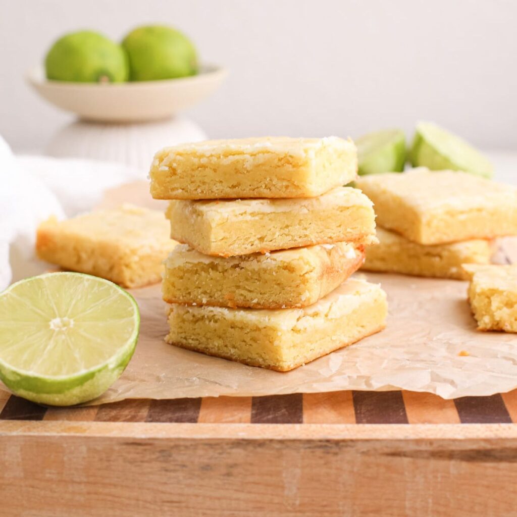 A stack of lime blondies on a cutting board next to fresh limes.