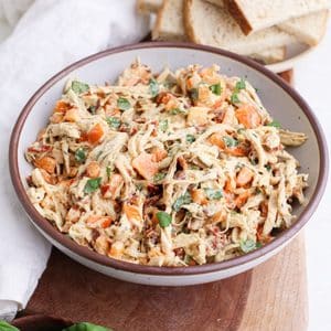 A bowl of marry me chicken salad with diced orange bell pepper and fresh basil leaves next to slices of toasted bread.
